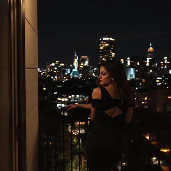 Woman in Black Dress on Balcony at Night: Elegant Scene